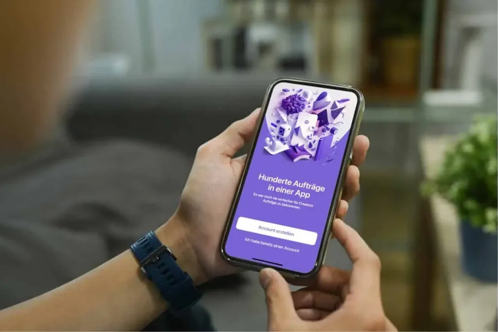 Hands hold a phone showing the Speekly start screen: “Hundreds of jobs in one app” and a Create account button