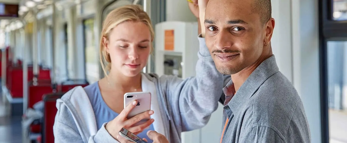 Zwei junge Fahrgäste in einer Stadtbahn schauen gemeinsam auf ein Smartphone