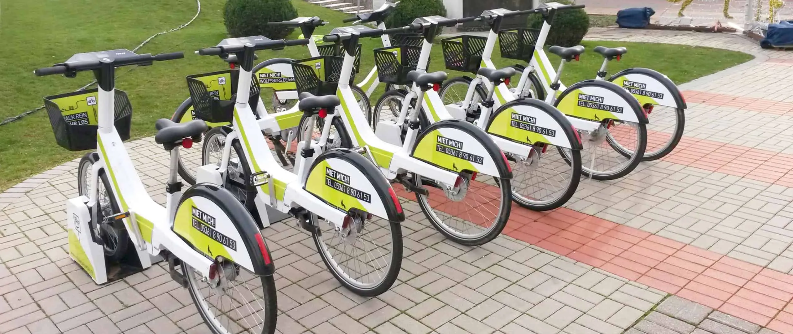 Reihe weiß-grüner Leih-Pedelecs mit „Miet mich!“-Aufklebern auf einem gepflasterten Platz
