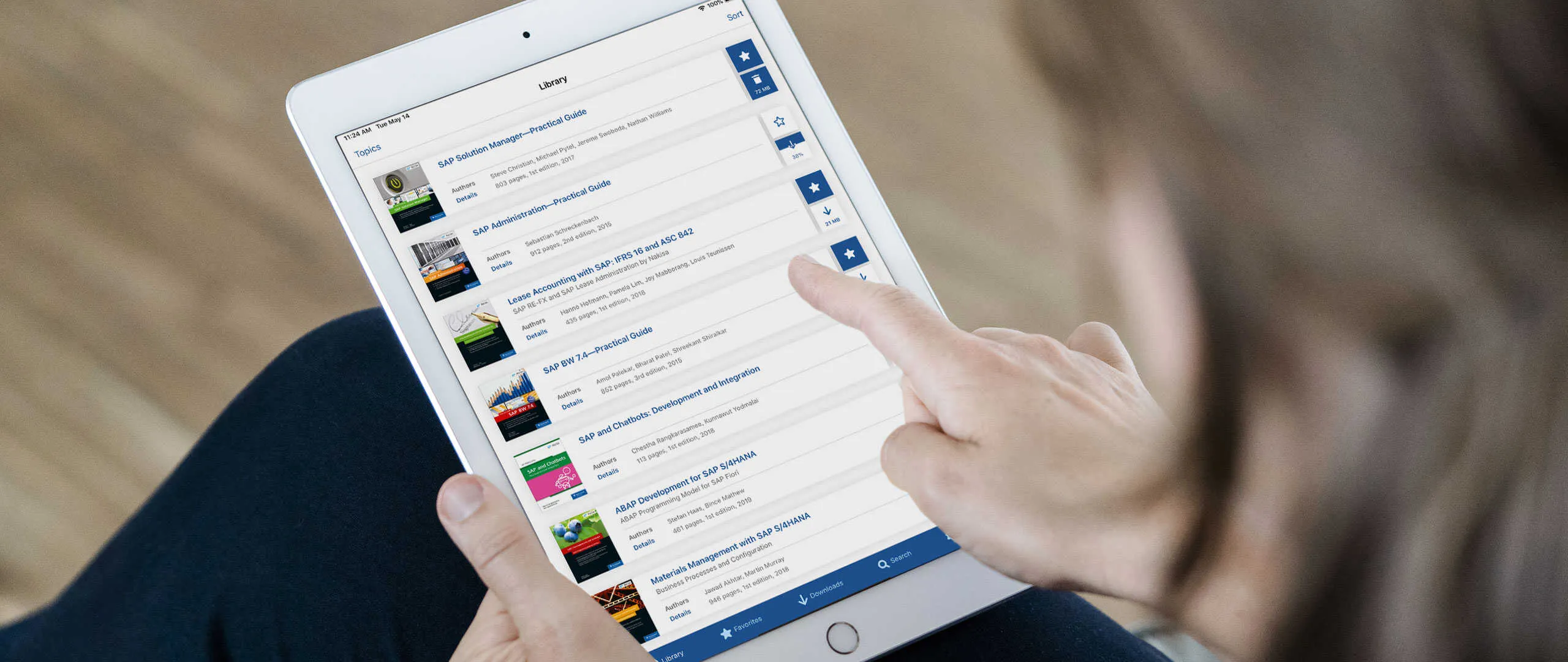 Person tippt auf einem Tablet in einer Bibliothek von SAP-Fachbüchern mit Autoren und Seitenzahlen