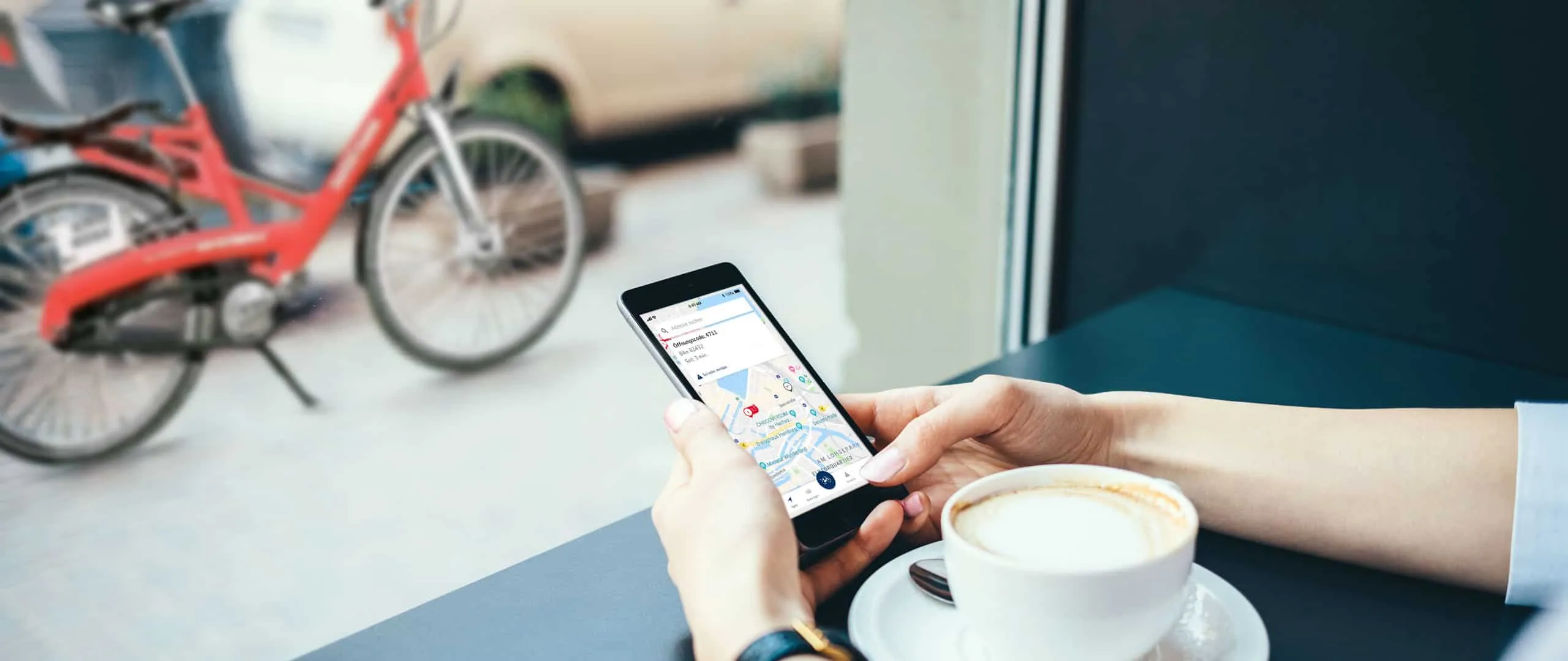 Person am Caféfenster bedient die App, draußen steht ein rotes StadtRAD-Leihrad