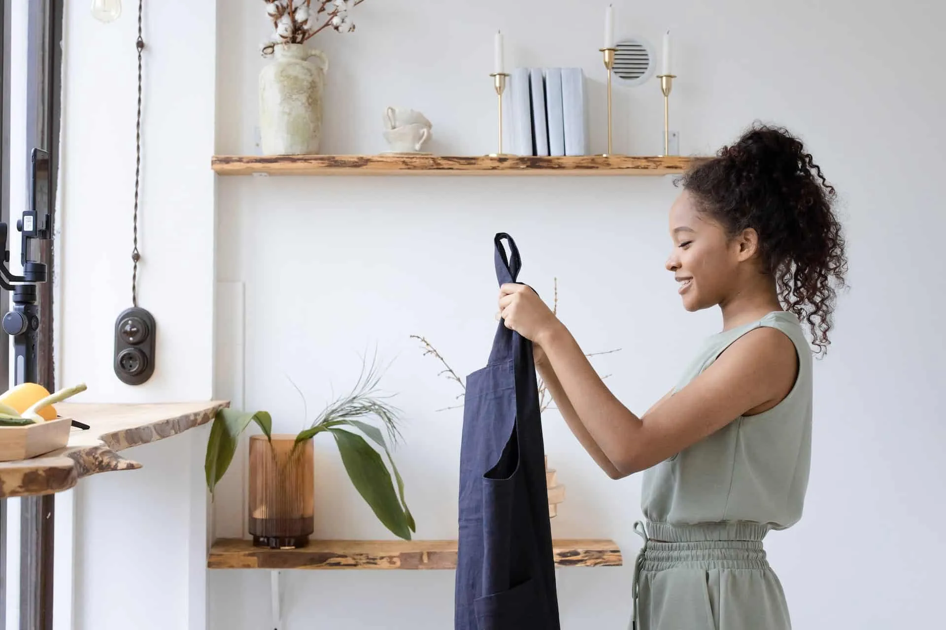 A content creator films a blue apron at home using a phone on a gimbal